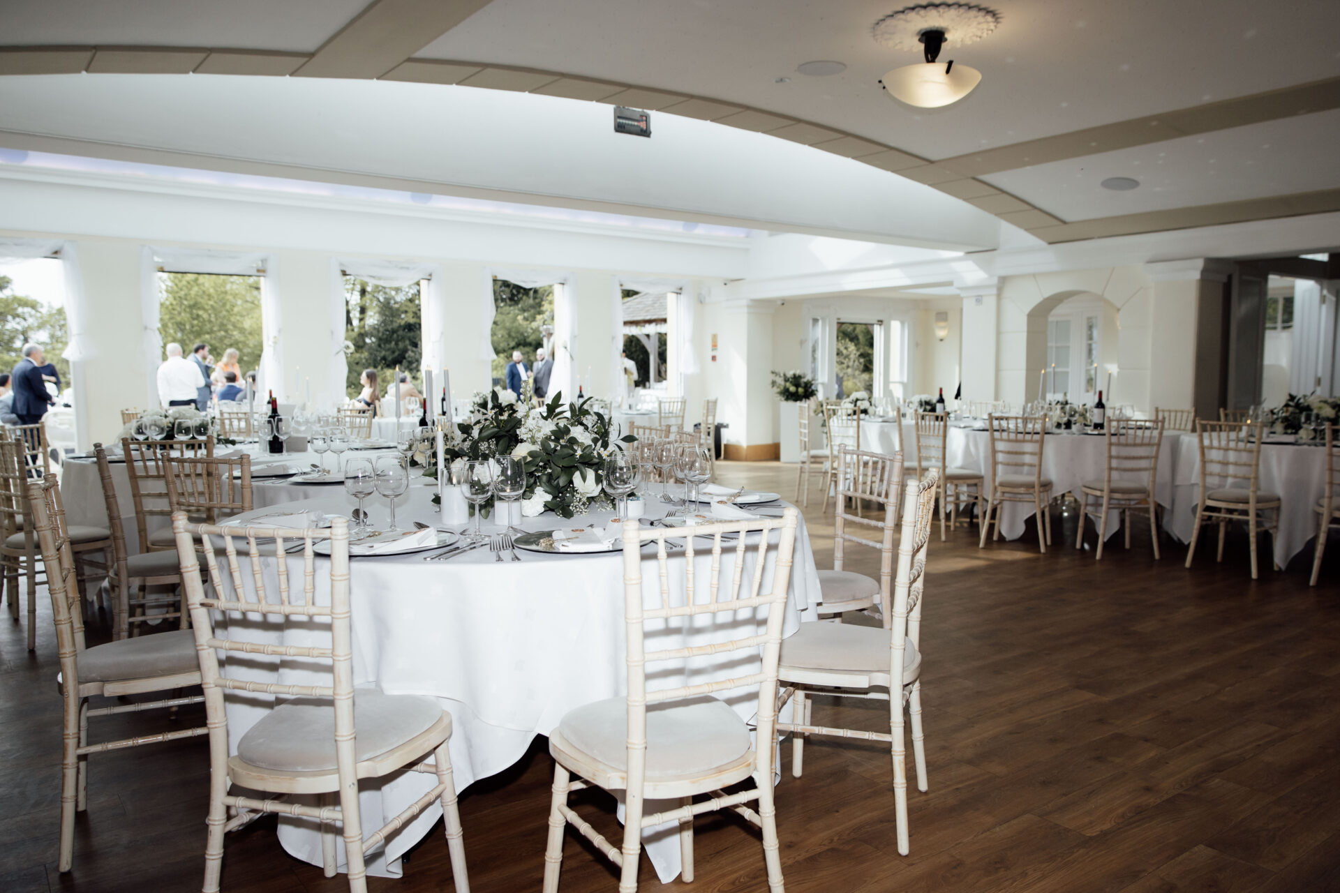 A large room with white wooden chairs and set tables.