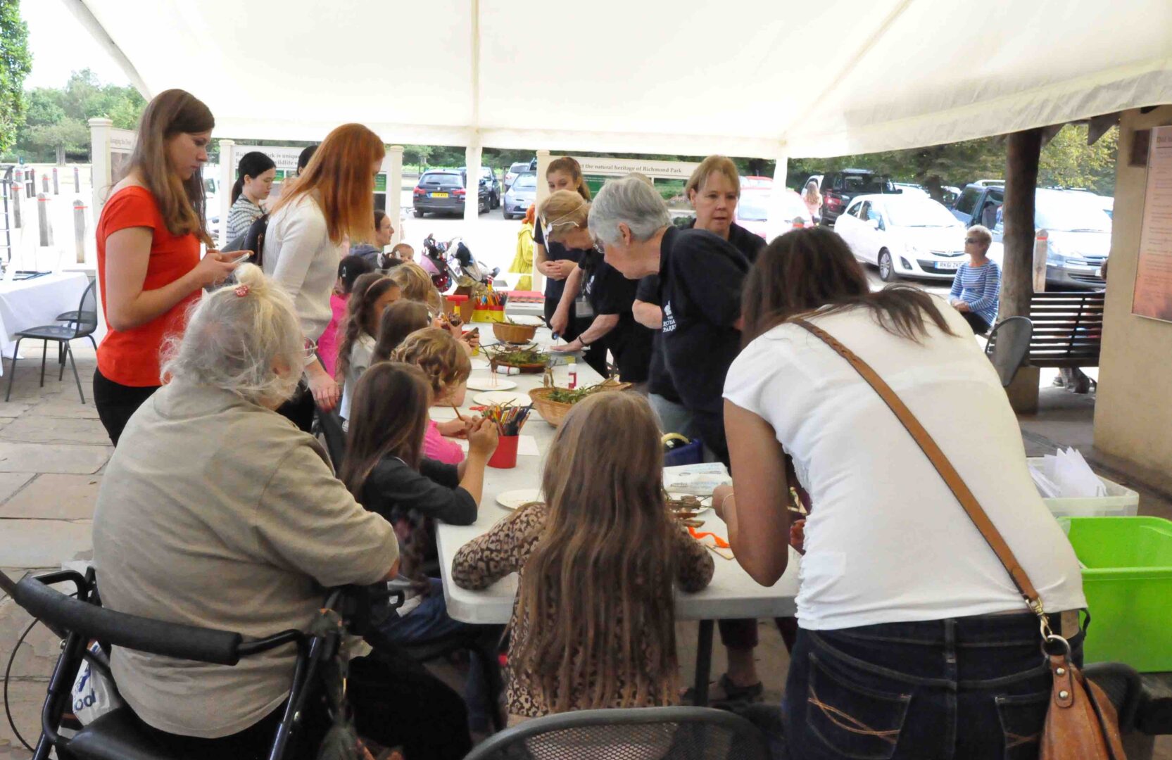 A group of people gathering around a craft table under a white marquee tent.