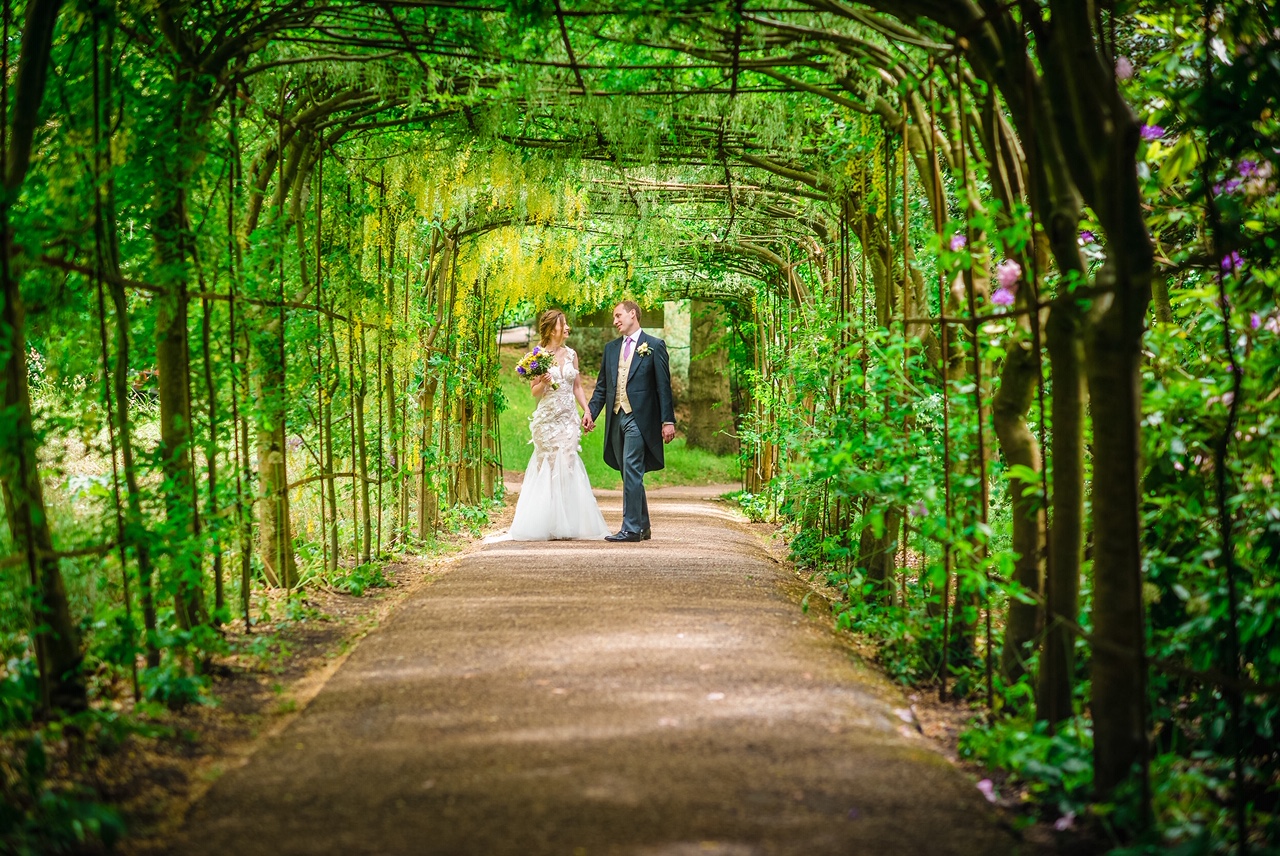 A bride and groom holding hands at the bottom of a leafy green archway.