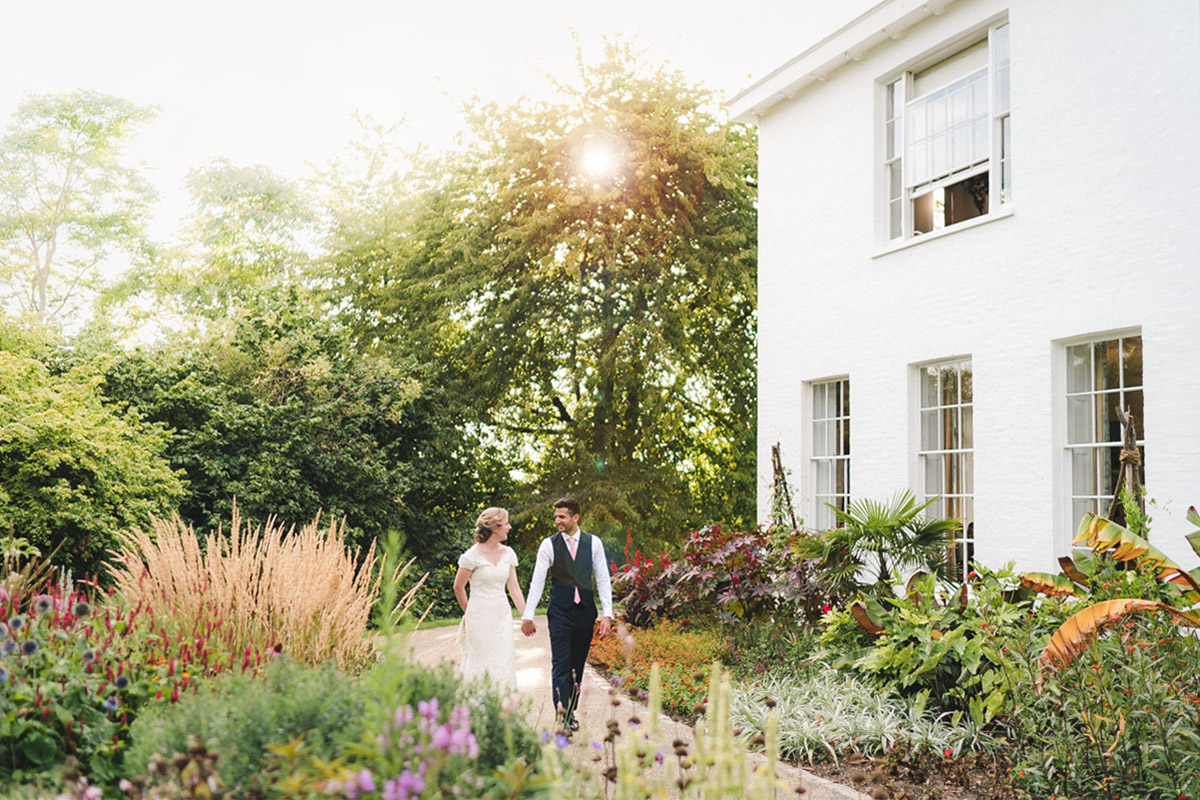 A couple in wedding attire holding hands and walking through an ornate garden.