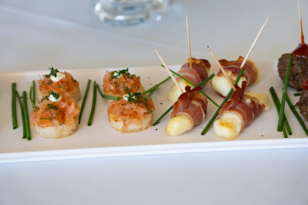 A white square plate with various hors d'oeuvres and chives.