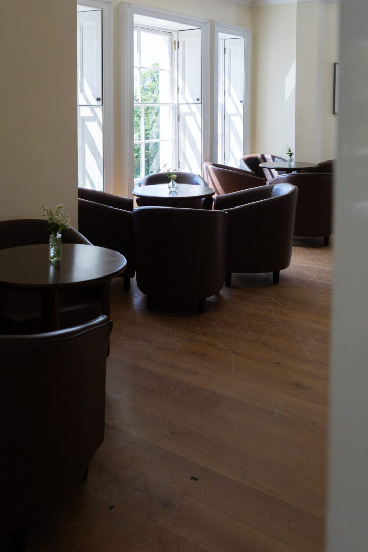 A large brightly lit room with dark leather chairs and wooden tables.