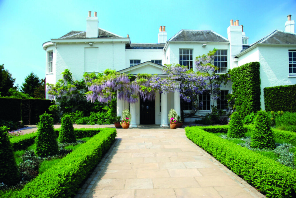 A large Georgian house with trimmed hedges and Wisteria surrounding the entrance.