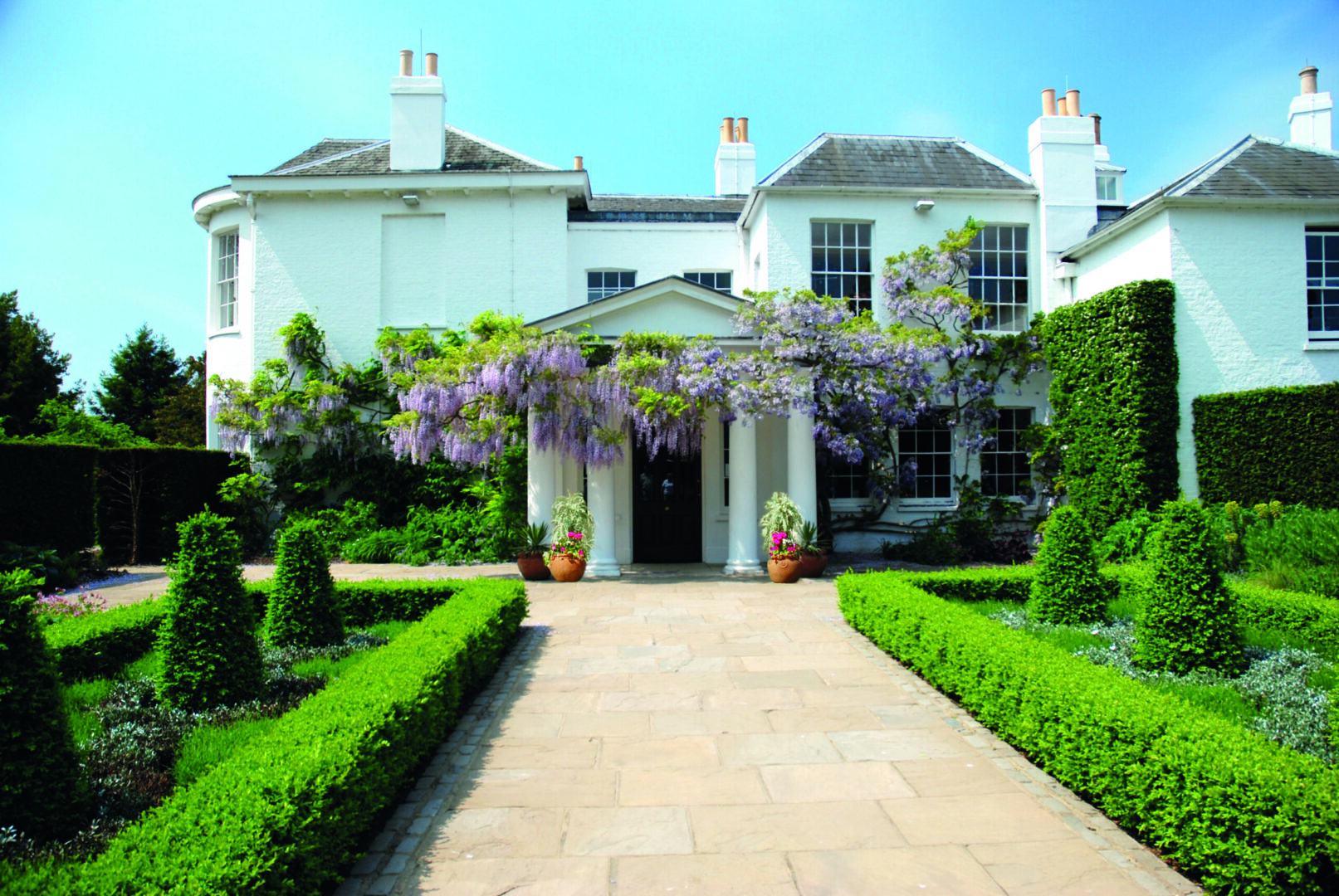 A large Georgian house with trimmed hedges and Wisteria surrounding the entrance.