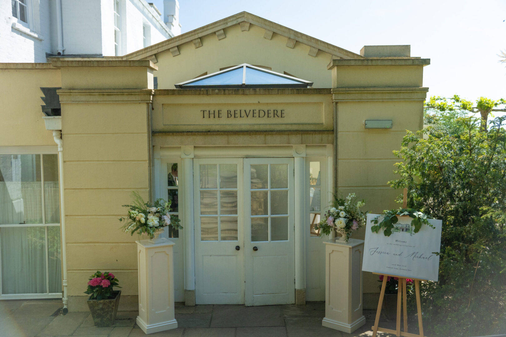 Ornate doors with "The Belvedere" above and podiums with bouquets of flowers.