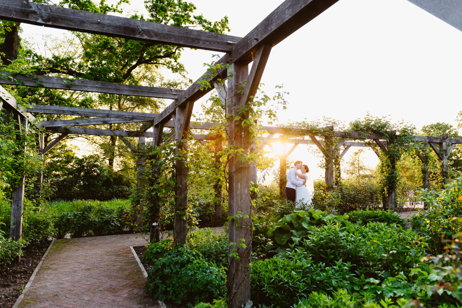 A bride and groom embracing in a vibrant garden at sunset.