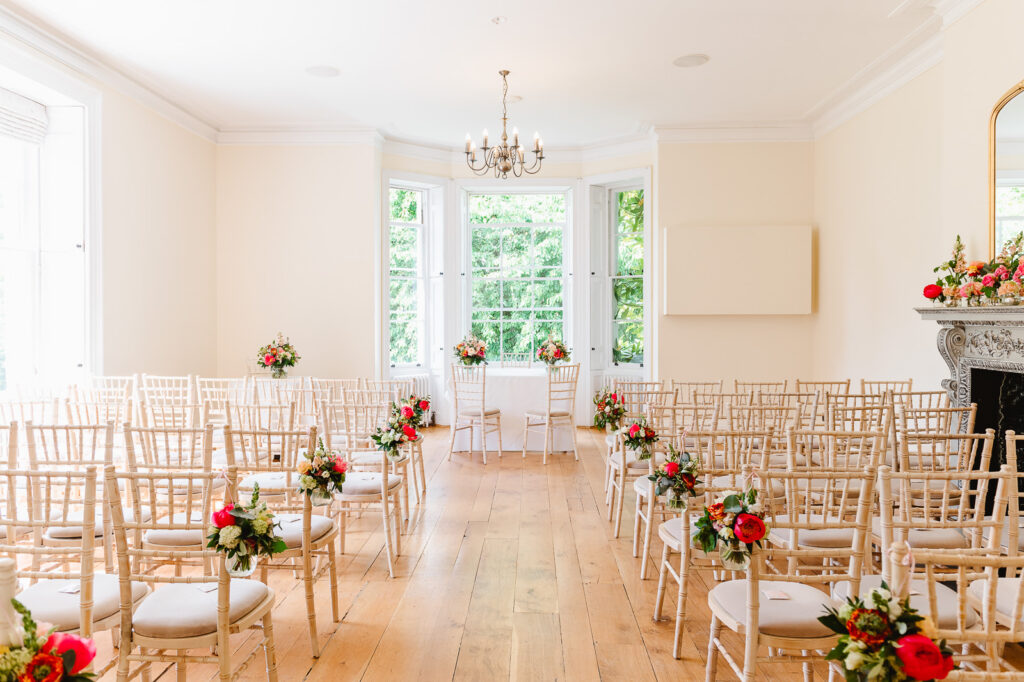 A large airy room with rows of light wooden chairs and bright pink flowers.