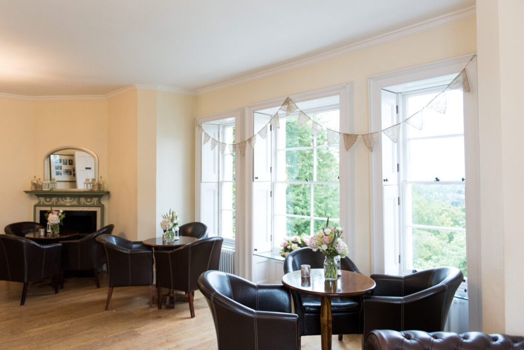 A large room with wooden floors, bright windows and brown leather chairs arranged around tables.