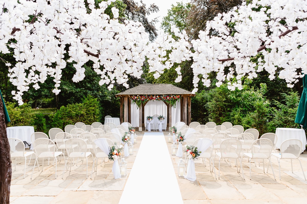 A floral wedding arch with white chairs on a patio.
