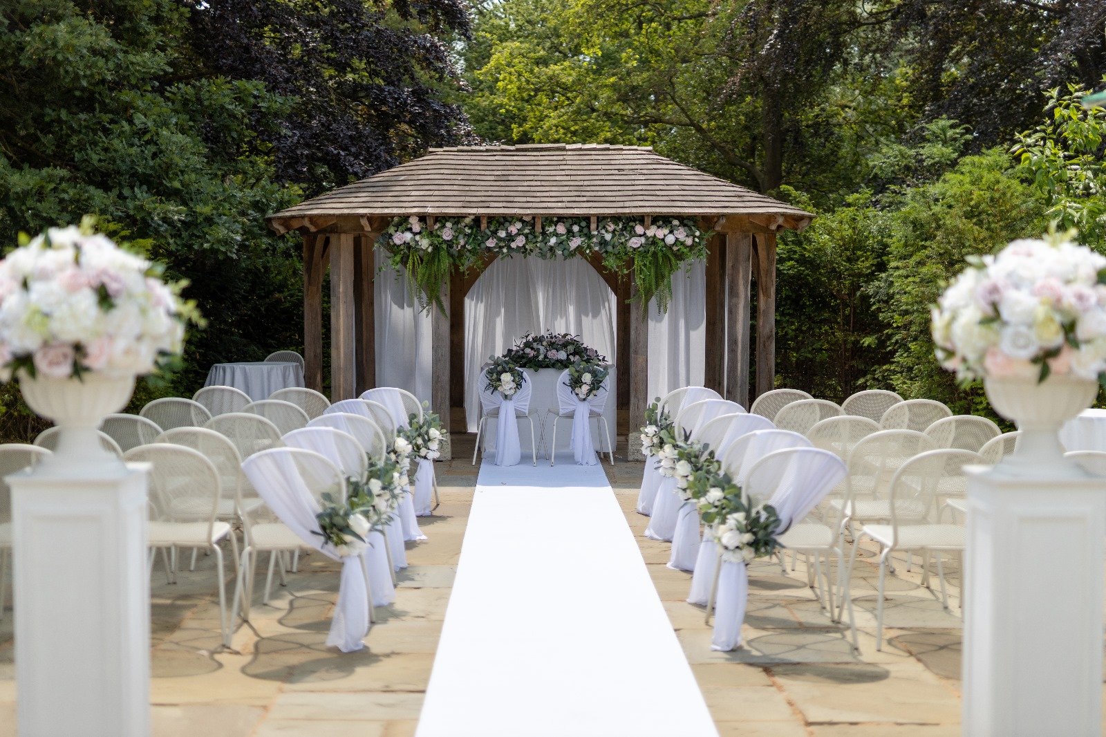 A wwedding arch with flowers and rows of white chairs in a patio area.
